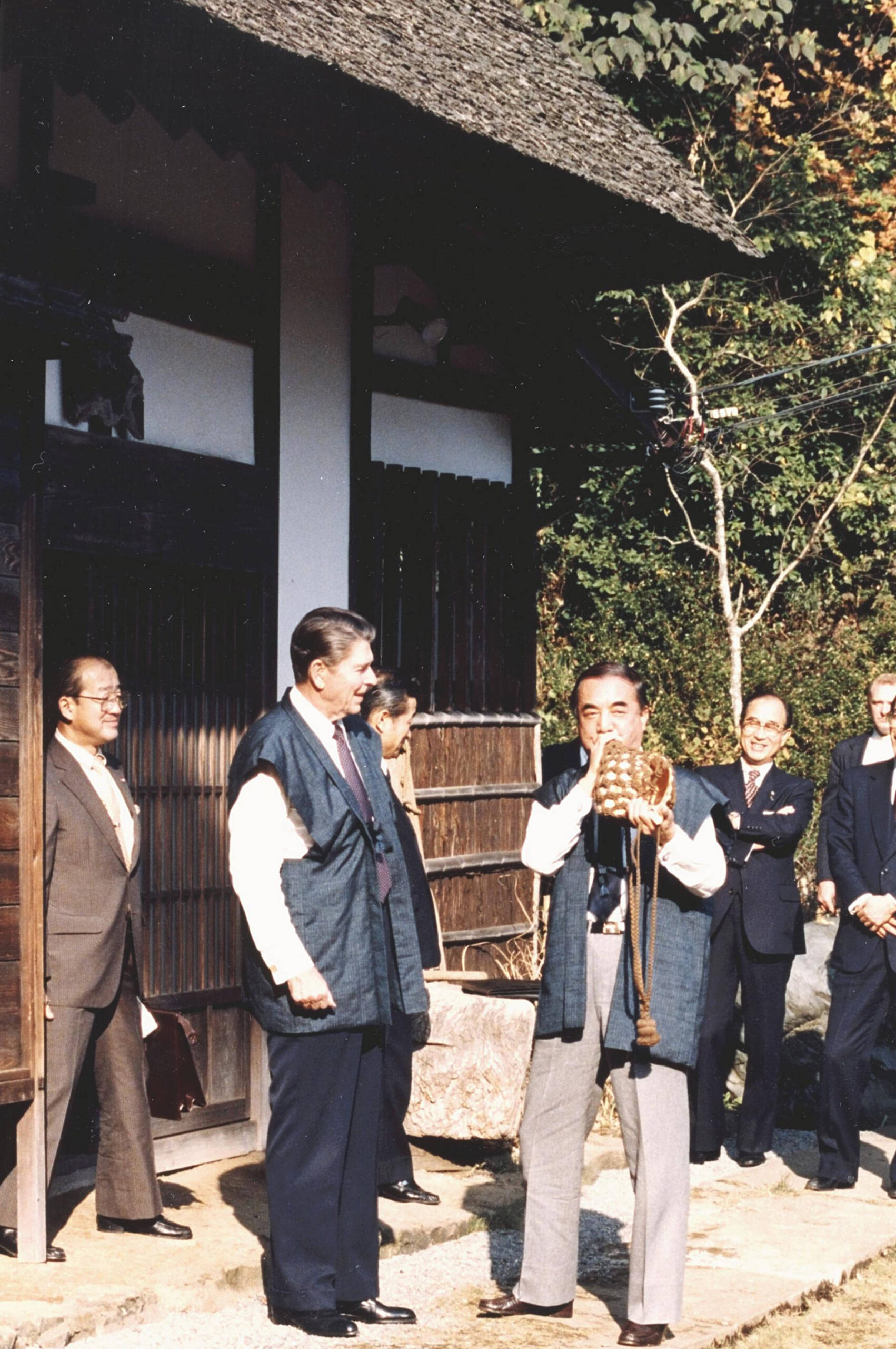 Yasuhiro Nakasone sopla en una caracola mientras el presidente estadounidense Ronald Reagan escucha en la villa de Nakasone en Tokio en noviembre de 1983. © The Yomiuri Shimbun vía AP Images