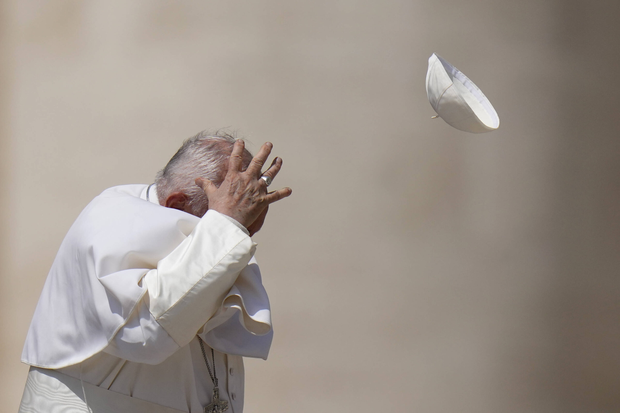 El papa Francisco intenta atrapar su solideo mientras el viento se lo lleva tras su audiencia general semanal en la Plaza de San Pedro del Vaticano el miércoles 15 de mayo de 2024. © Photo AP/Alessandra Tarantino