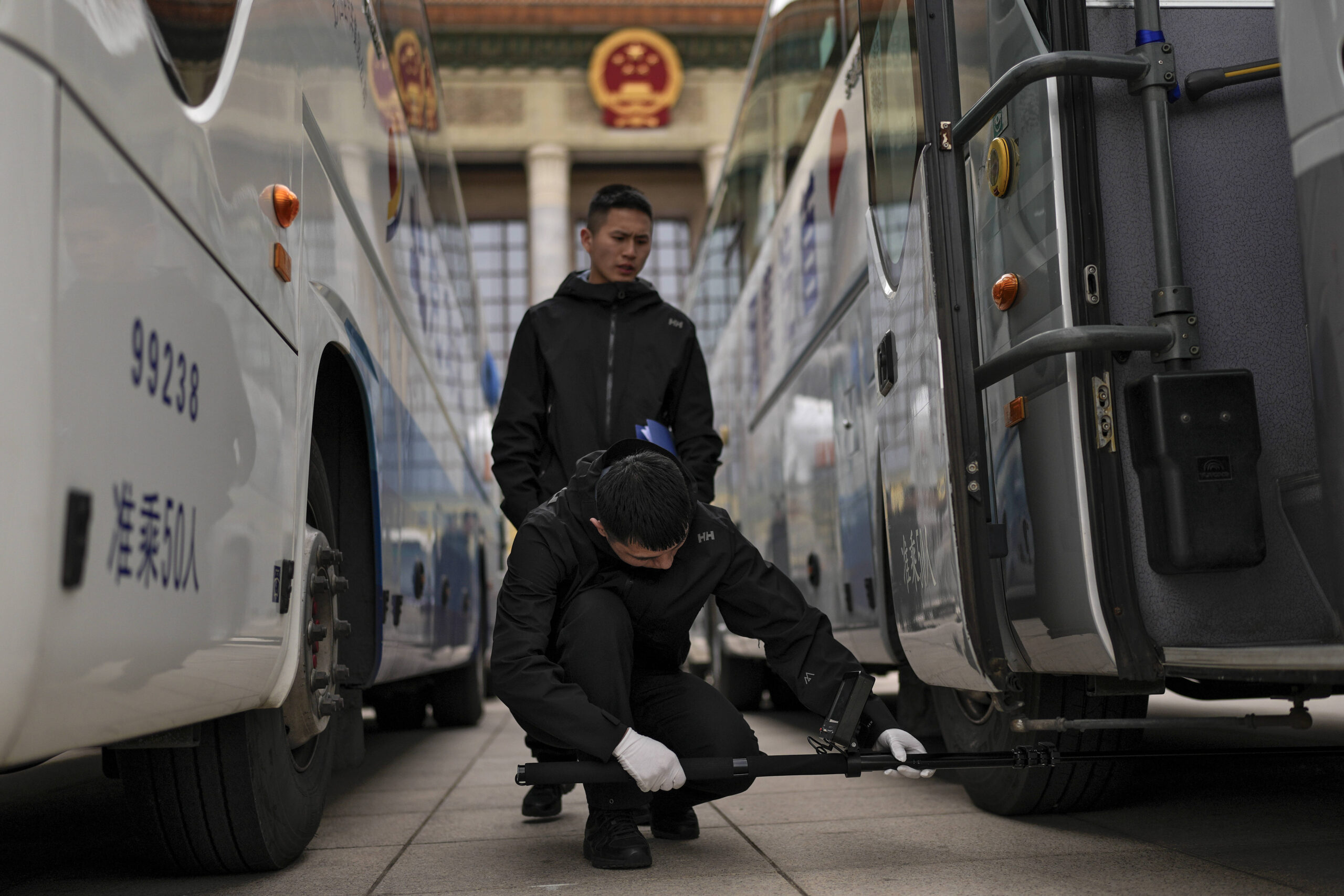 Miembros de la policía china y de las fuerzas especiales de la brigada antibombas utilizan un perro rastreador y un dispositivo especial para inspeccionar los autobuses aparcados en el Gran Palacio del Pueblo durante una rueda de prensa previa a la apertura de la Conferencia Consultiva Política del Pueblo Chino en Pekín, el lunes 3 de marzo de 2025. © Photo AP/Andy Wong