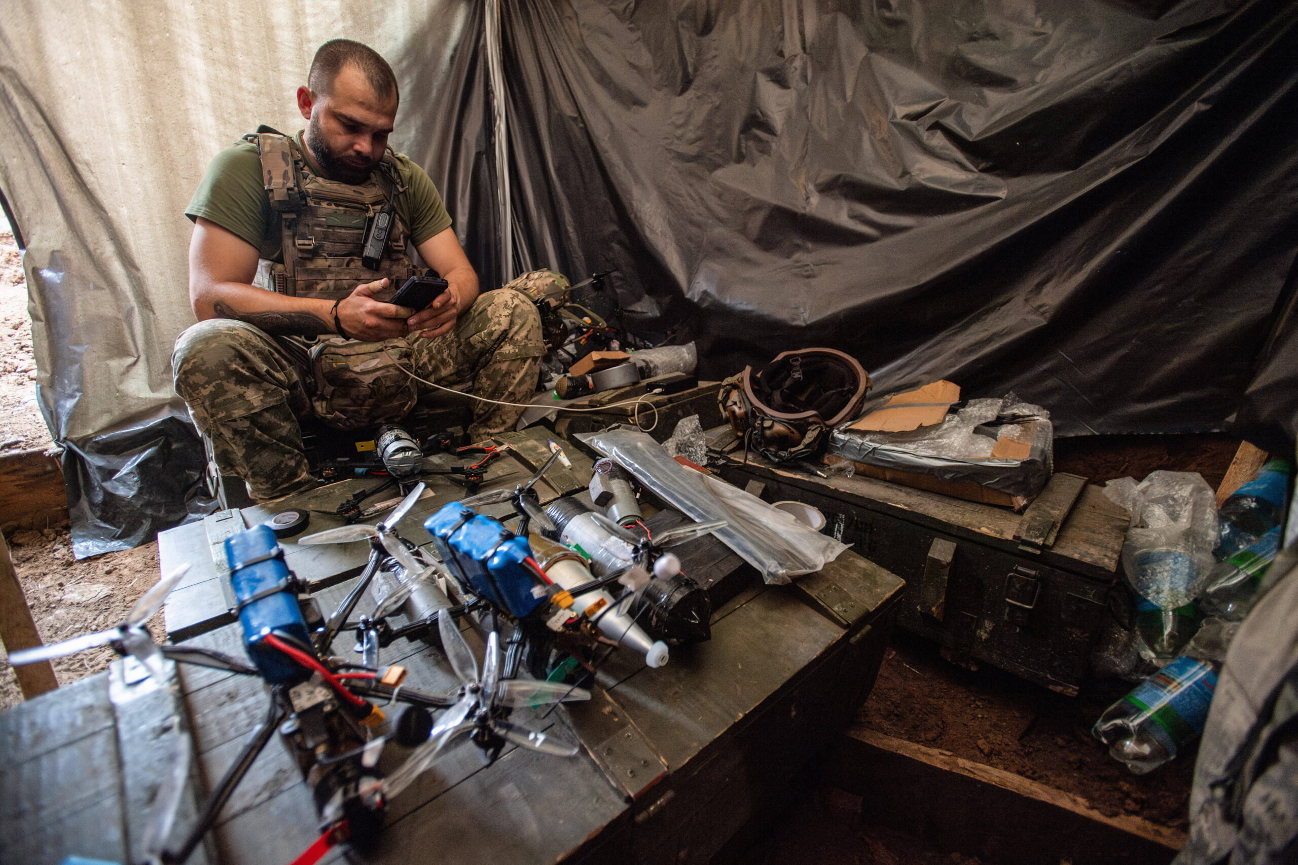 Un soldado ucraniano de la brigada 92 mira su teléfono mientras está sentado frente a drones FPV equipados con explosivos, a unos 10 kilómetros de la frontera con Rusia, en la región de Járkov, Ucrania. Foto de Laurel Chor (SOPA Images).