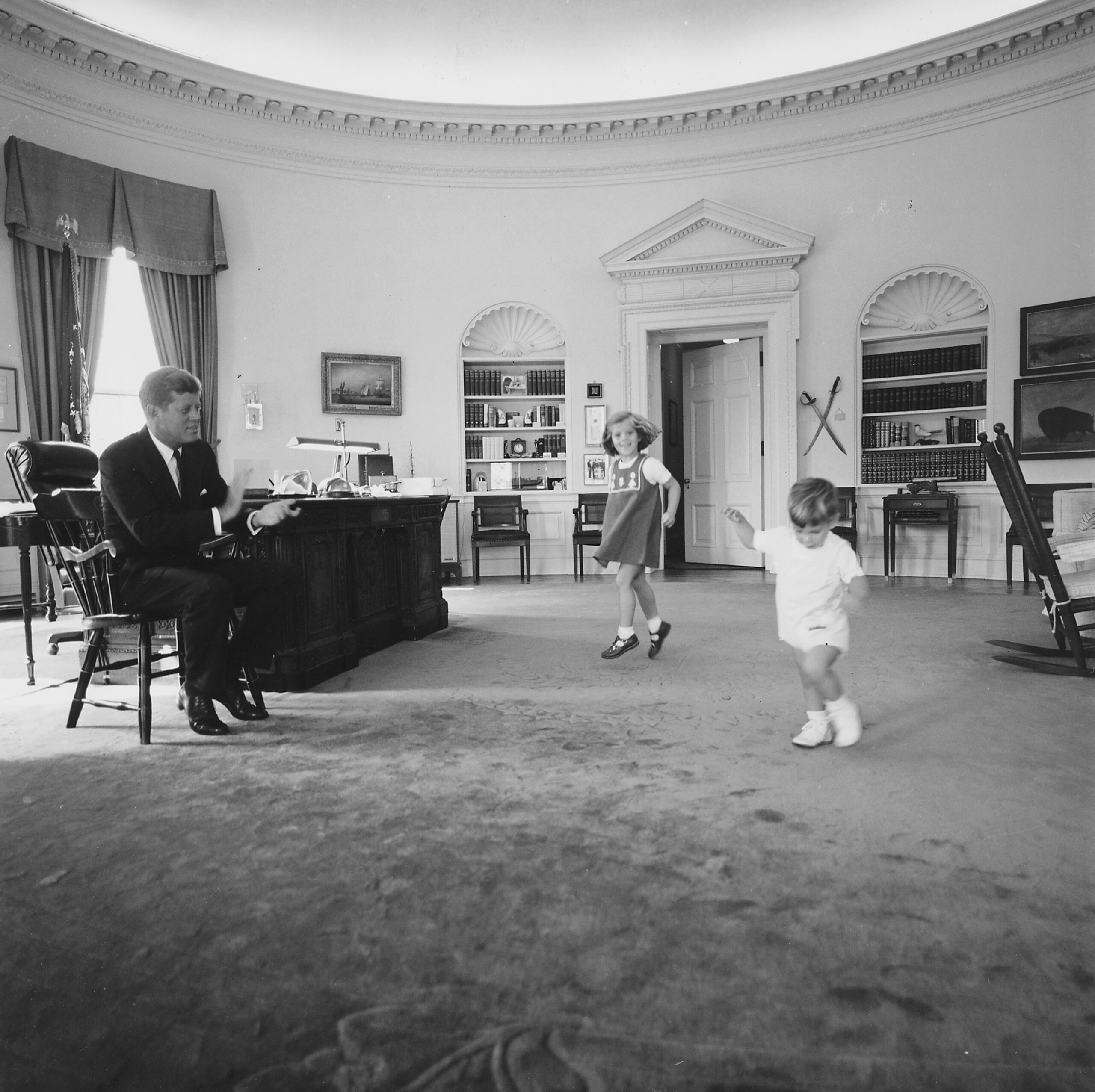 Caroline Kennedy y John F. Kennedy Jr. jugando en el Despacho Oval bajo la mirada de su padre, el 10 de octubre de 1962. © Cecil Stoughton/Biblioteca y Museo Presidencial John F. Kennedy/NARA
