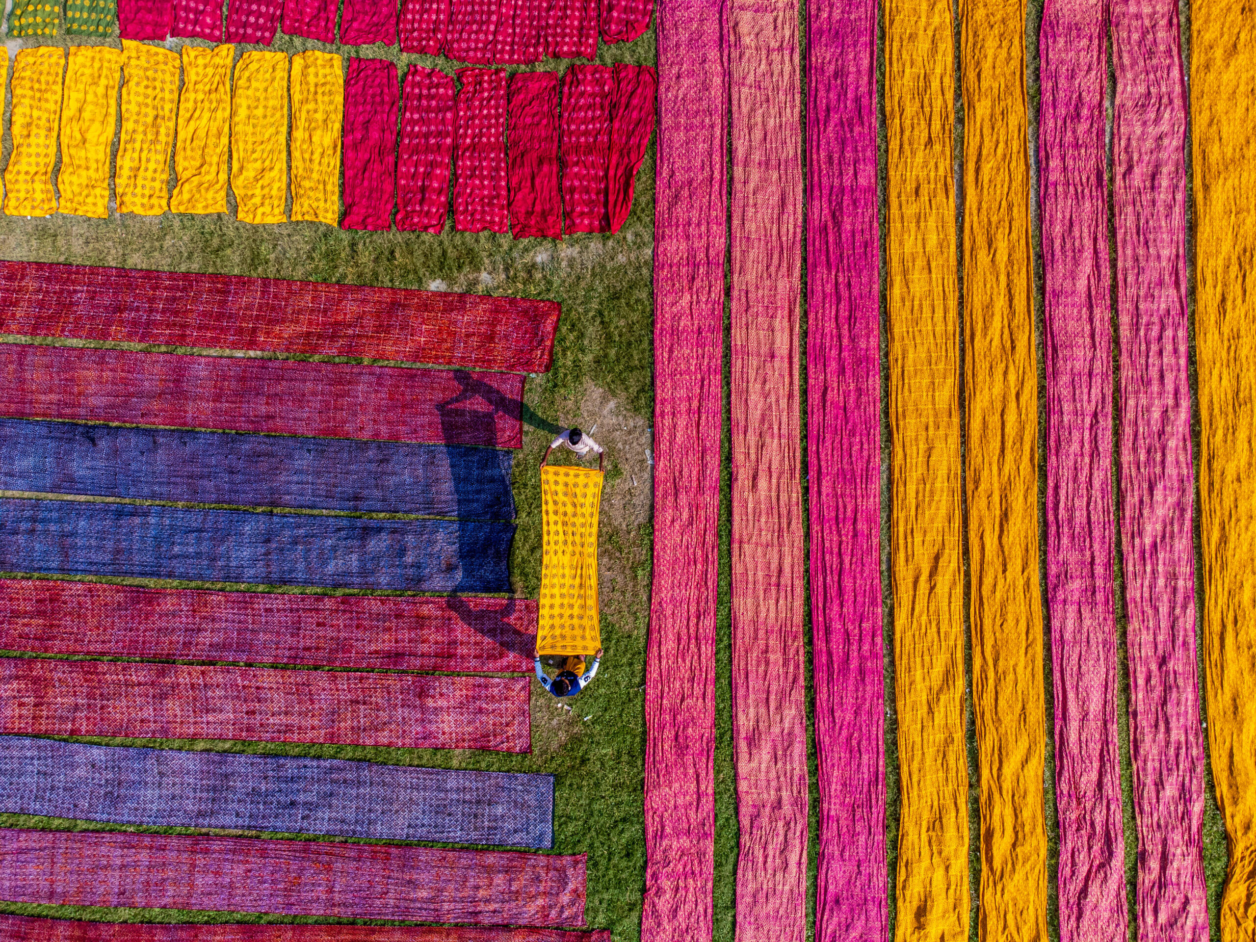 Trabajadores extienden telas de vivos colores para que se sequen al sol, en un campo de la aldea de Batik, en Bangladesh, en noviembre de 2025. © Bipul Ahmed/Solent News/SIPA  