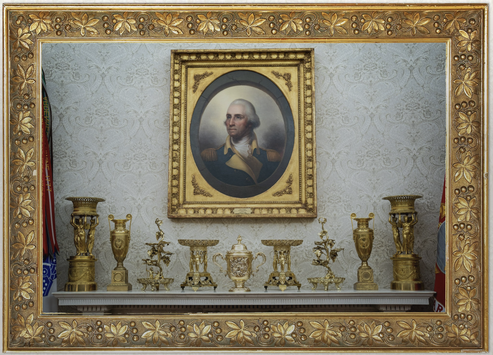La hilera de objetos dorados de la repisa de la chimenea del Despacho Oval, bajo el retrato de George Washington pintado por Rembrandt Peale: cestas con cariátides, jarrones de estilo Imperio, copas y jarras de vermeil y bronce dorado. Imagen extraída de la investigación del Washington Post.