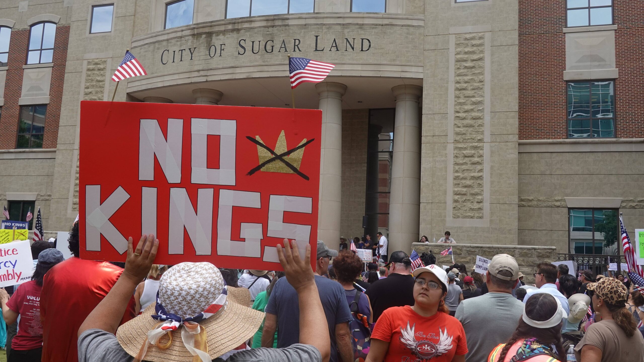 Frente al ayuntamiento de Sugar Land, en Texas, la corona tachada se exhibe entre dos banderas estadounidenses: en este estado, en el que Trump se ha impuesto en dos ocasiones, la protesta recurre a los emblemas patrióticos. Foto: Xu Jianmei / Xinhua