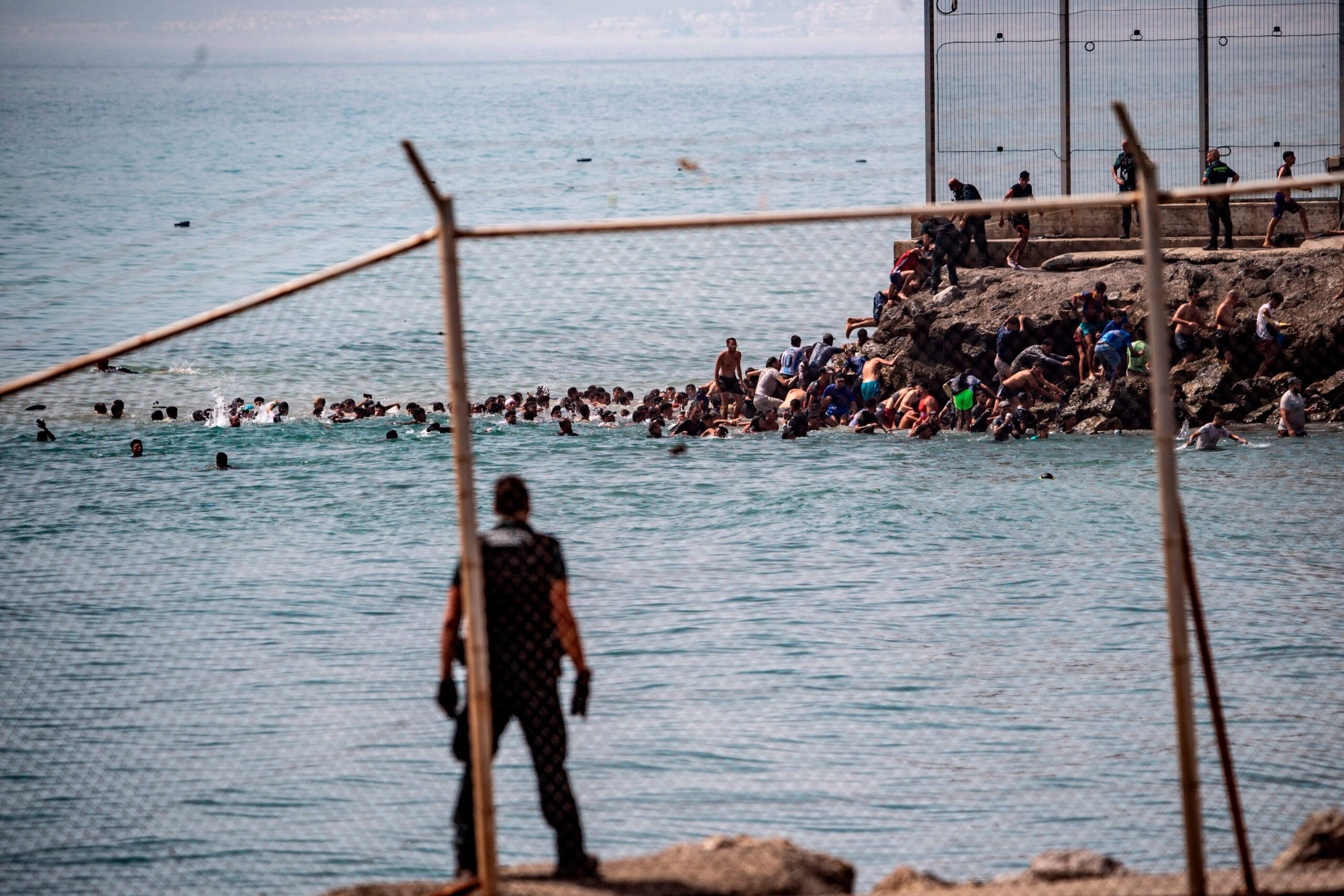 Vista a través de la valla fronteriza: bajo la mirada de los agentes, decenas de nadadores rodeaban el extremo de la valla para llegar a las rocas de Ceuta, el jueves 30 de julio de 2026. © AP Photo/Antonio Sempere/SIPA