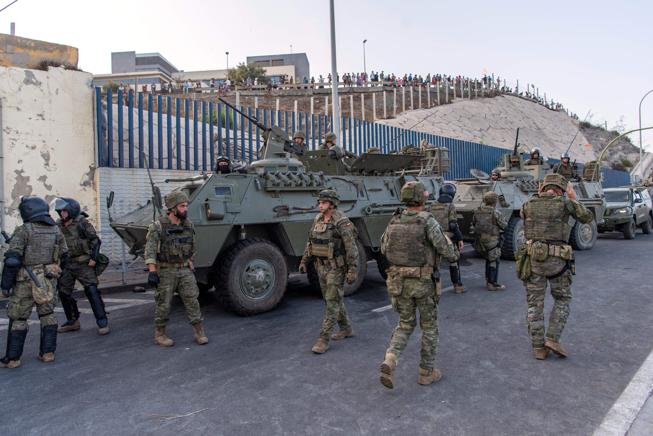El ejército español y sus vehículos blindados se despliegan a lo largo de la valla, el jueves 30 de julio, ante la mirada de una multitud congregada en el lado marroquí. © AP Photo/Antonio Sempere/SIPA