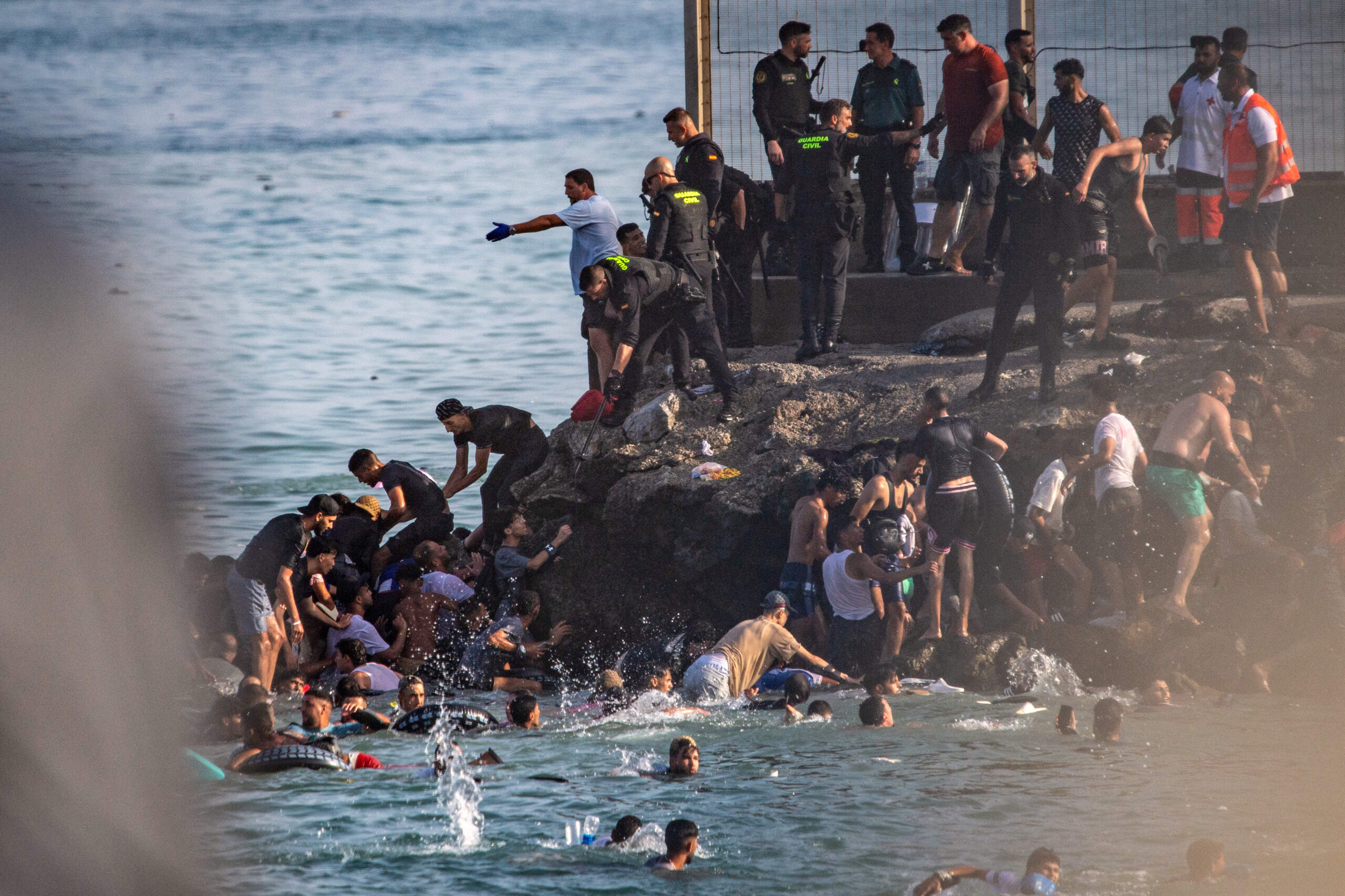 Sobre las rocas del muelle, la frontera se convierte en una operación de rescate: la Guardia Civil y la Cruz Roja ayudan a sacar del agua a los migrantes tras la travesía. © AP Photo/Antonio Sempere/SIPA
