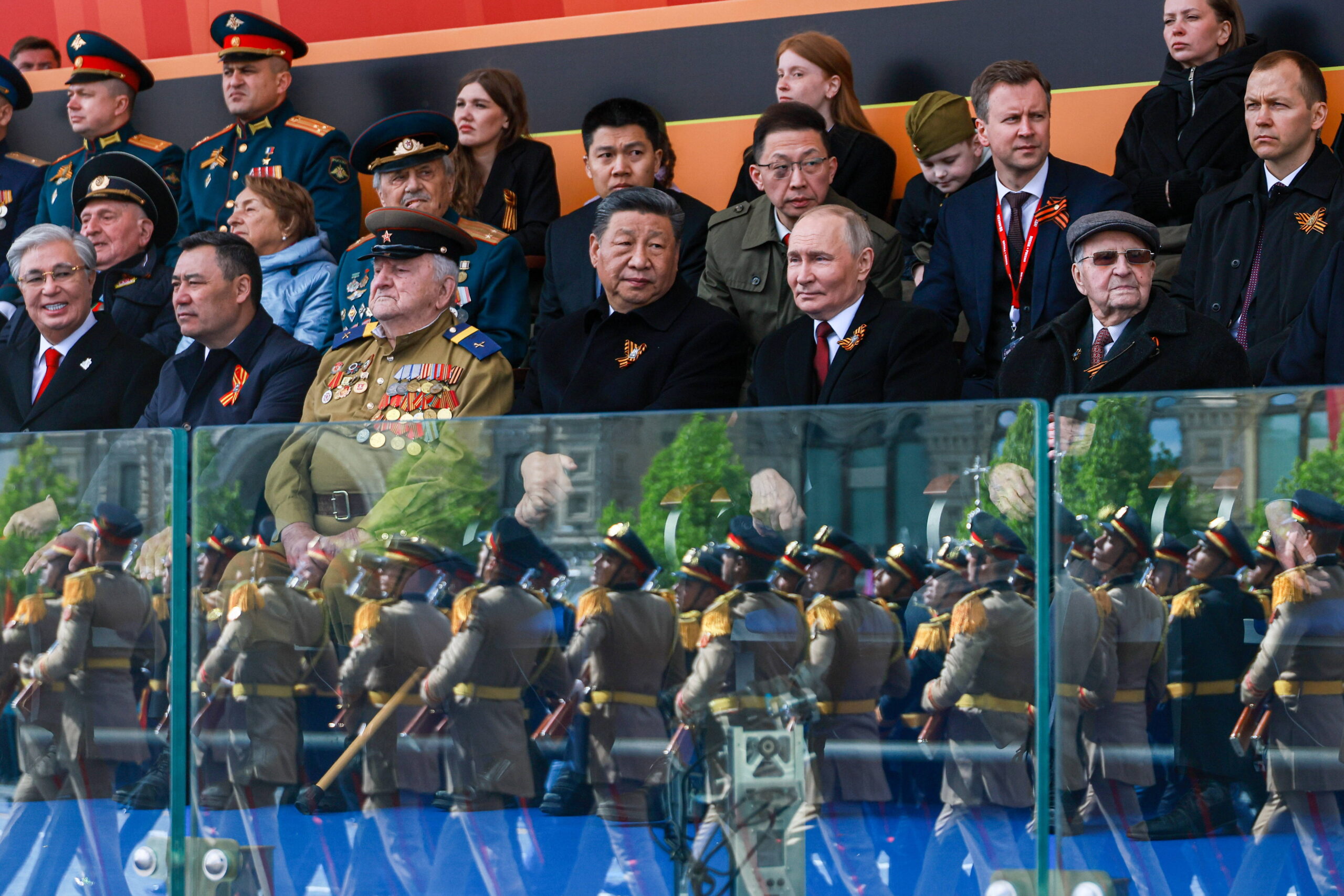 Xi Jinping y Vladimir Putin, uno al lado del otro en la primera fila de la tribuna, flanqueados por veteranos condecorados y otros funcionarios, mientras el desfile se refleja en el cristal protector. Foto: Vladimir Smirnov / ZUMA