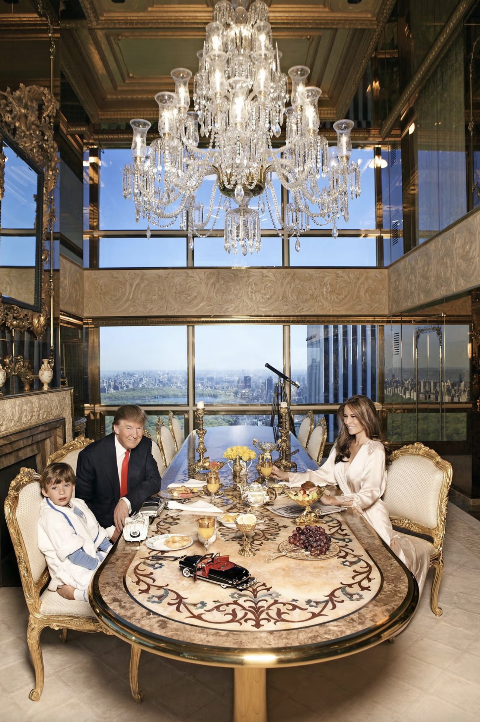 Donald Trump, Melania y Barron desayunando en el comedor del ático: mesa con tablero de mármol con incrustaciones, sillas doradas, lámpara de araña de cristal y ventanales con vistas a Central Park. Régine Mahaux/MT