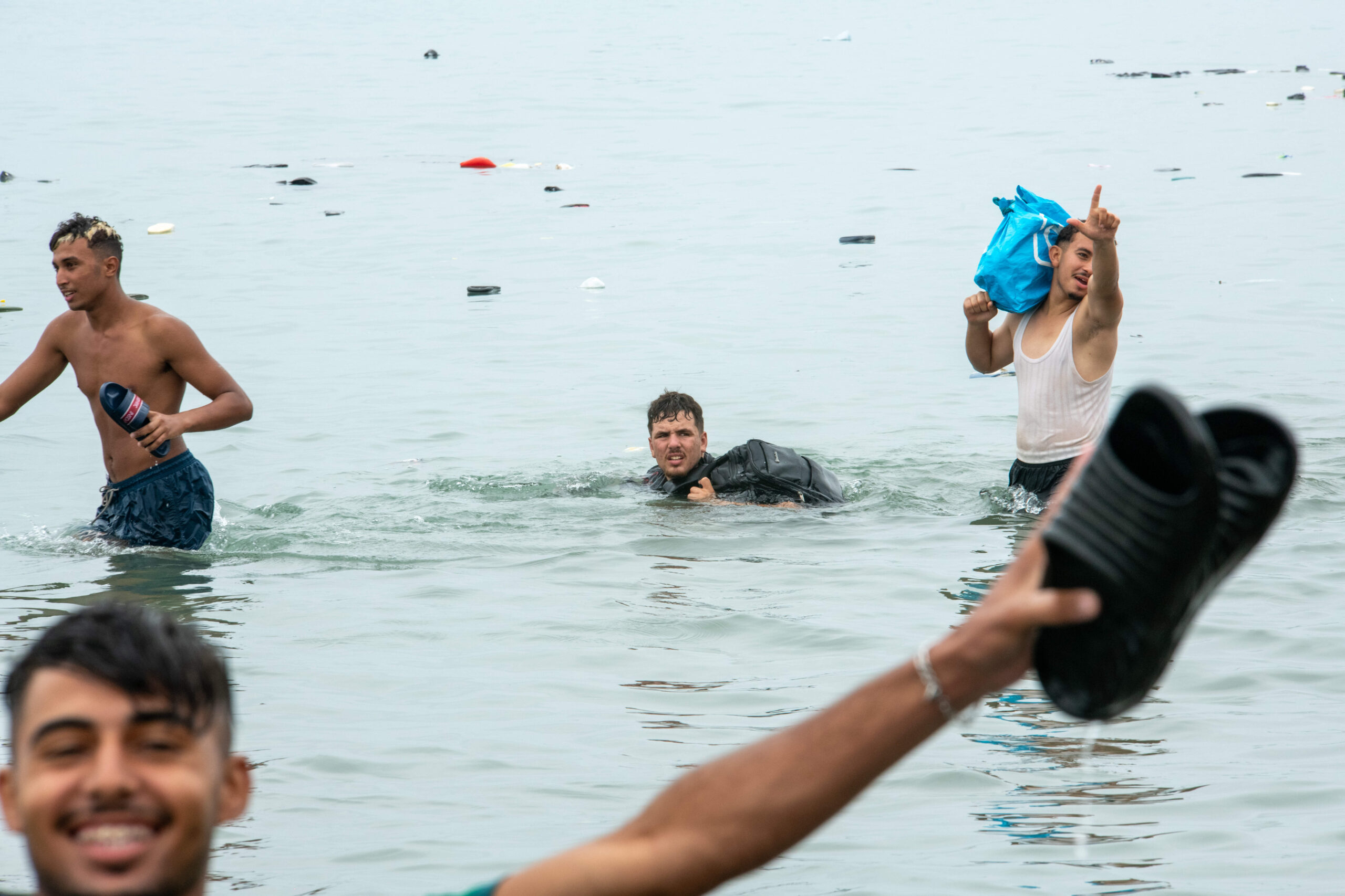 Un hombre nada hacia Ceuta, con la mochila fuera del agua, en medio de los objetos abandonados que van a la deriva por el estrecho, el 31 de julio de 2026. Foto: Juan Carlos Lucas