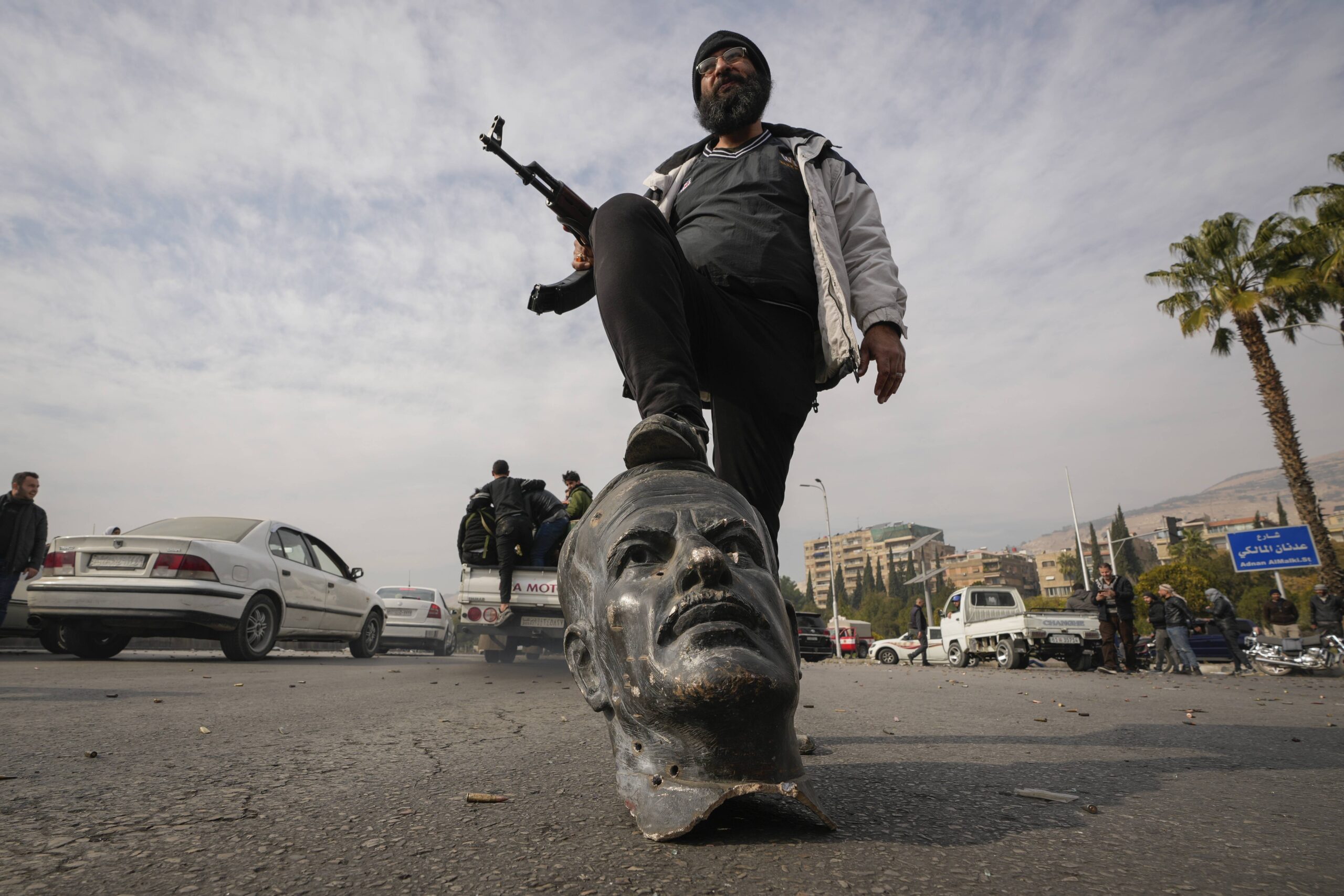 Un combattant de l'opposition marche sur un buste brisé du  président syrien Hafez el Assad à Damas, Syrie, dimanche 8 décembre 2024. © AP Photo/Hussein Malla