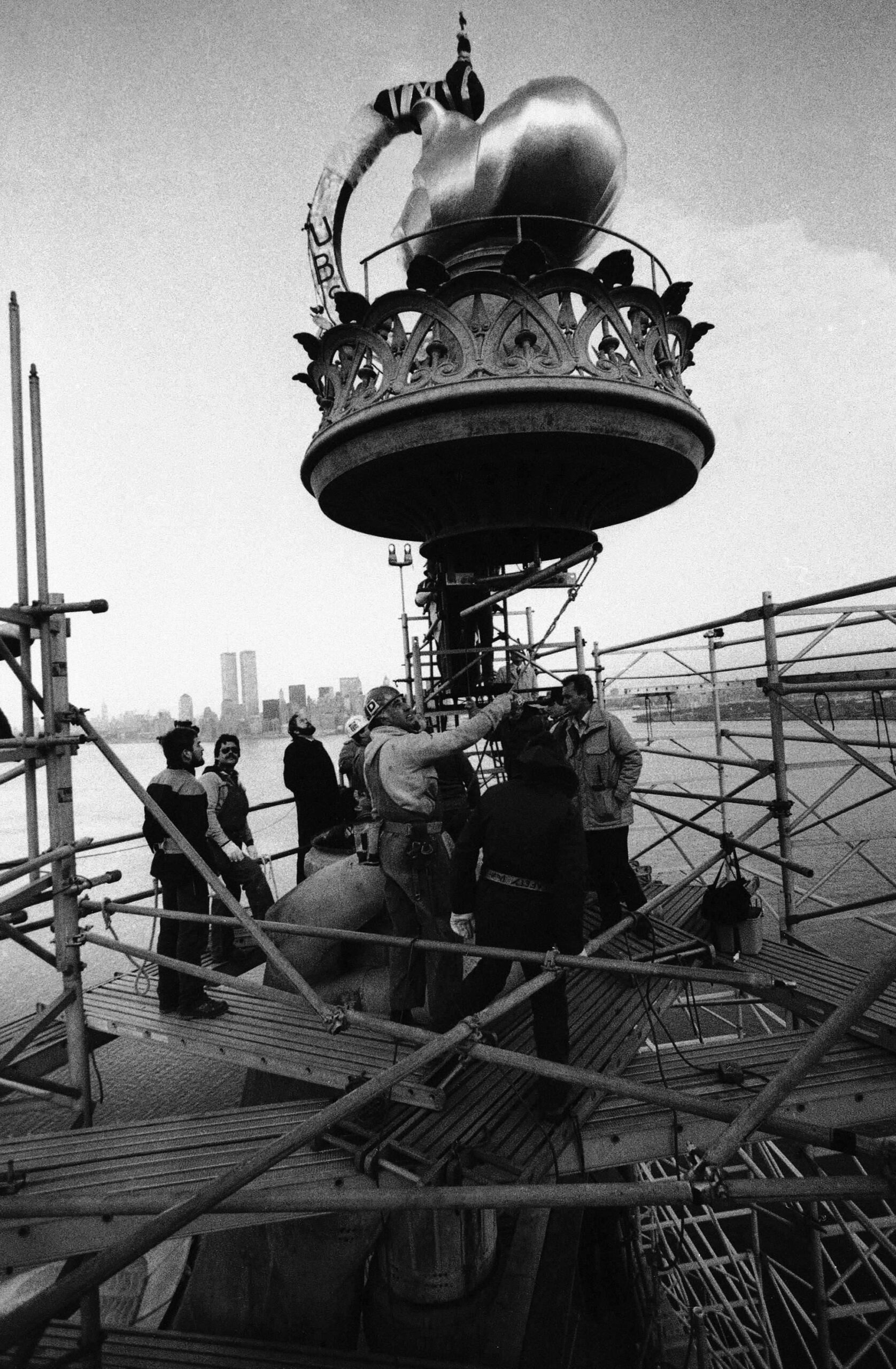 Des ouvriers assemblent la torche de la Statue de la Liberté au-dessus du port de New York, le 25 novembre 1985 pendant les travaux de remplacement de la flamme originale par une torche recouverte de feuilles d'or de 2,5 tonnes. © AP Photo