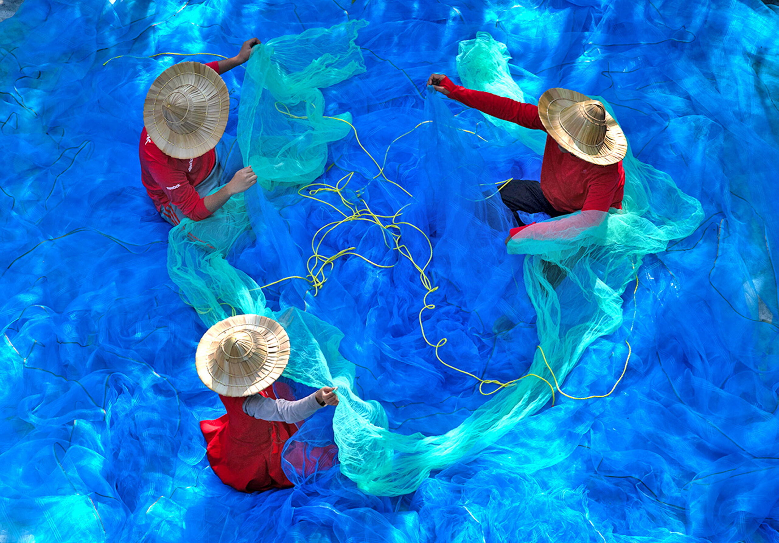 Des pêcheurs réparent leurs filets colorés afin de les préparer pour une nouvelle journée en mer, dans l'État du Bengale occidental, en Inde, en avril 2023. © Solent News/SIPA