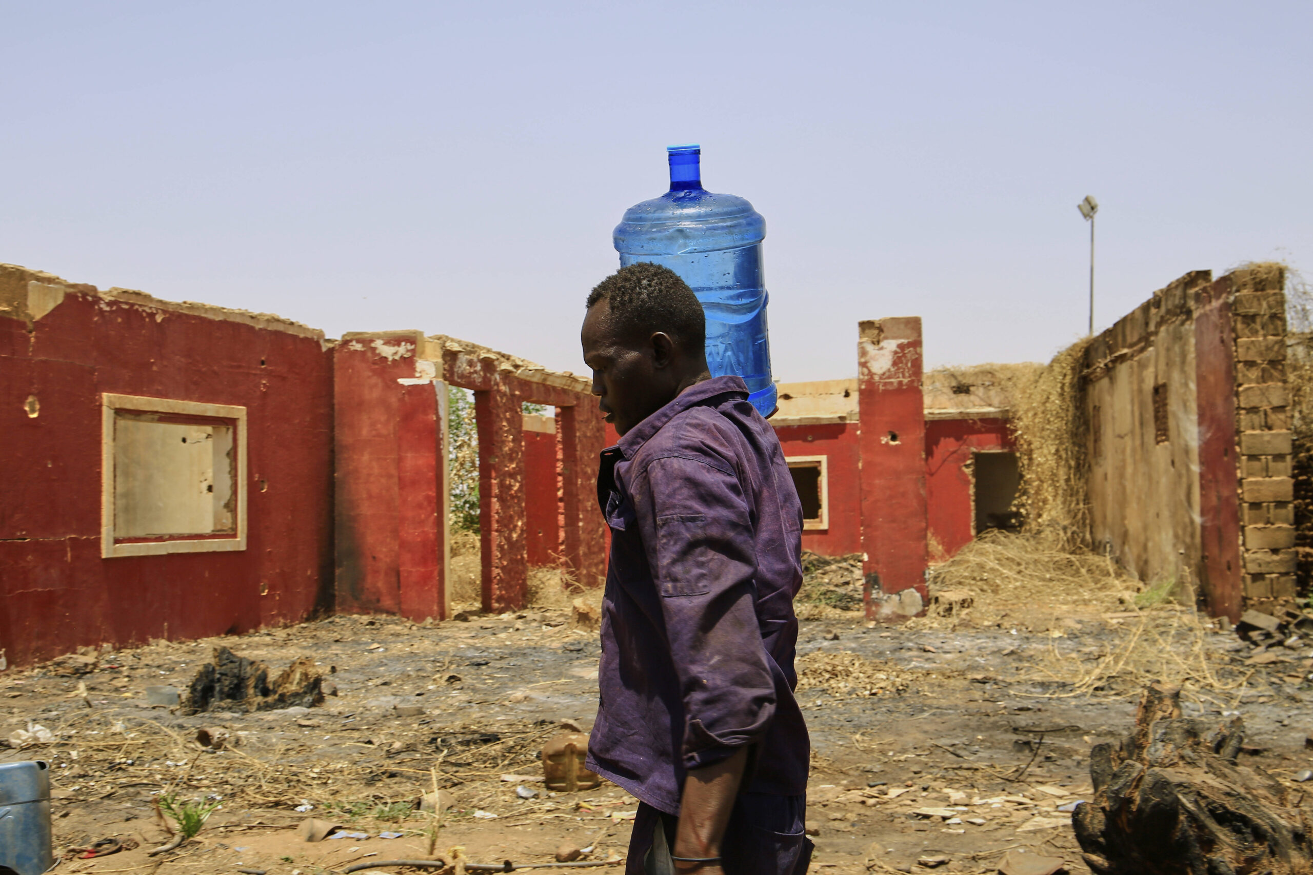 Un homme transporte un bidon d'eau devant un bâtiment endommagé pendant la guerre civile, à un point de distribution mis en place en raison des coupures d'eau à Khartoum, au Soudan, le dimanche 25 mai 2025. © AP Photo/Sipa