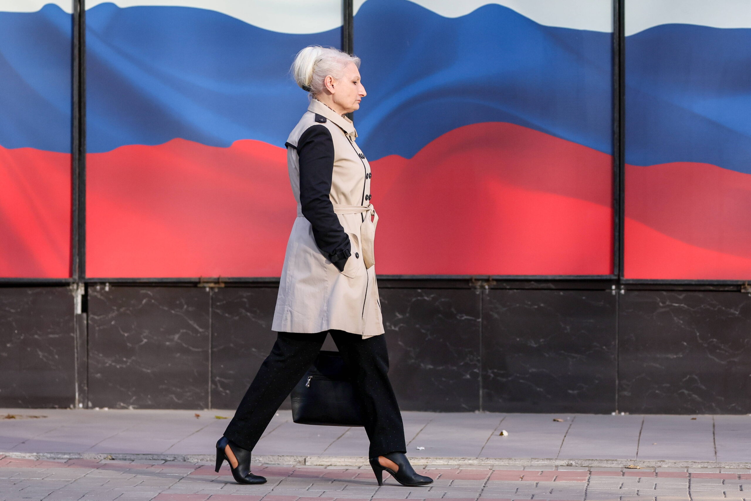 Le 23 octobre 2023, à Donetsk, ville située dans l'oblast ukrainien du même nom occupé par la Russie, une femme marche dans une rue devant des banderoles aux couleurs nationales russes. (© Yagodkin/TASS/Sipa USA) 