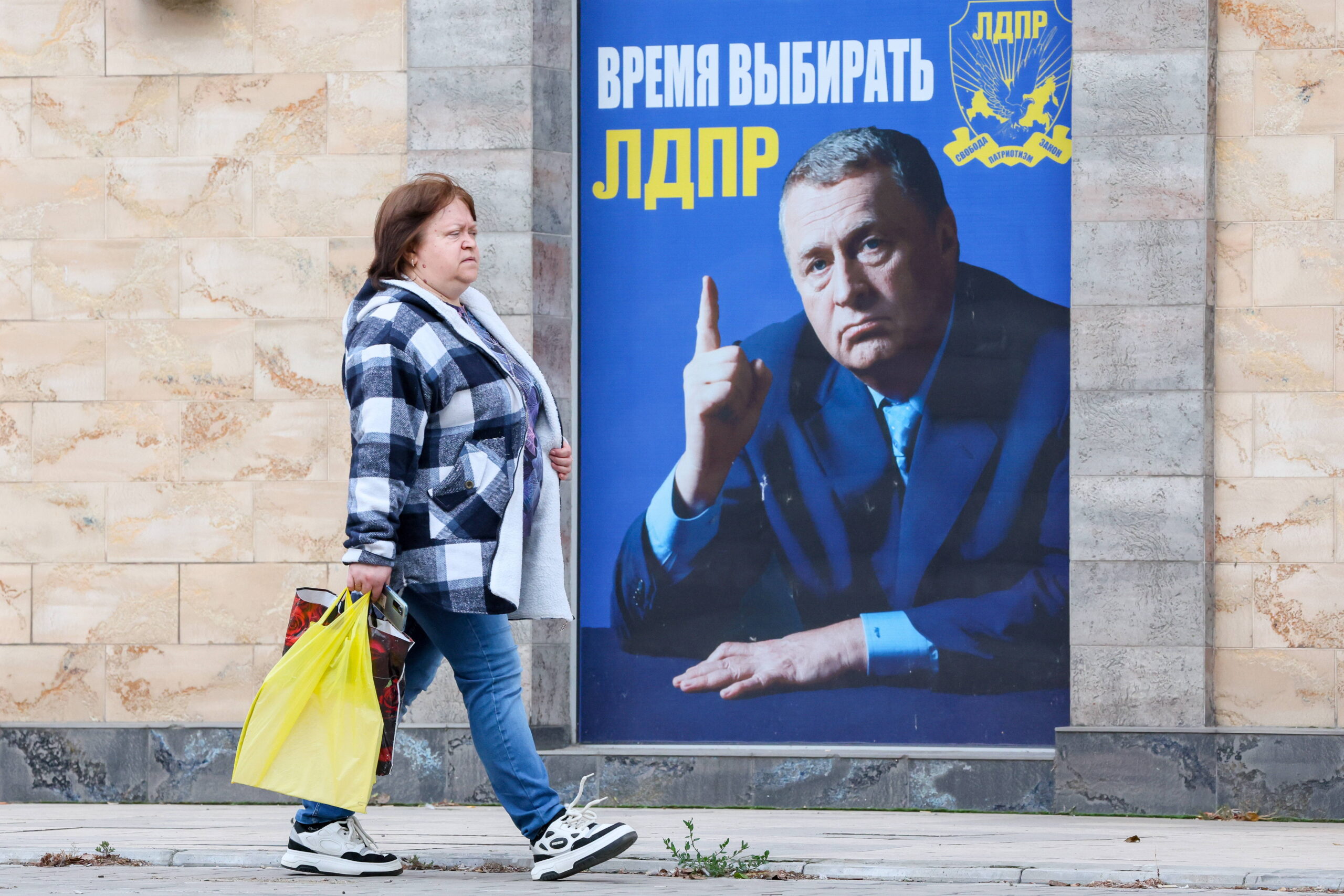 Le 23 octobre 2023, à Donetsk, ville située dans l'oblast ukrainien du même nom occupé par la Russie, une femme passe devant une banderole faisant la promotion du parti libéral-démocrate de Russie Dmitry (© Yagodkin/TASS/Sipa USA) 