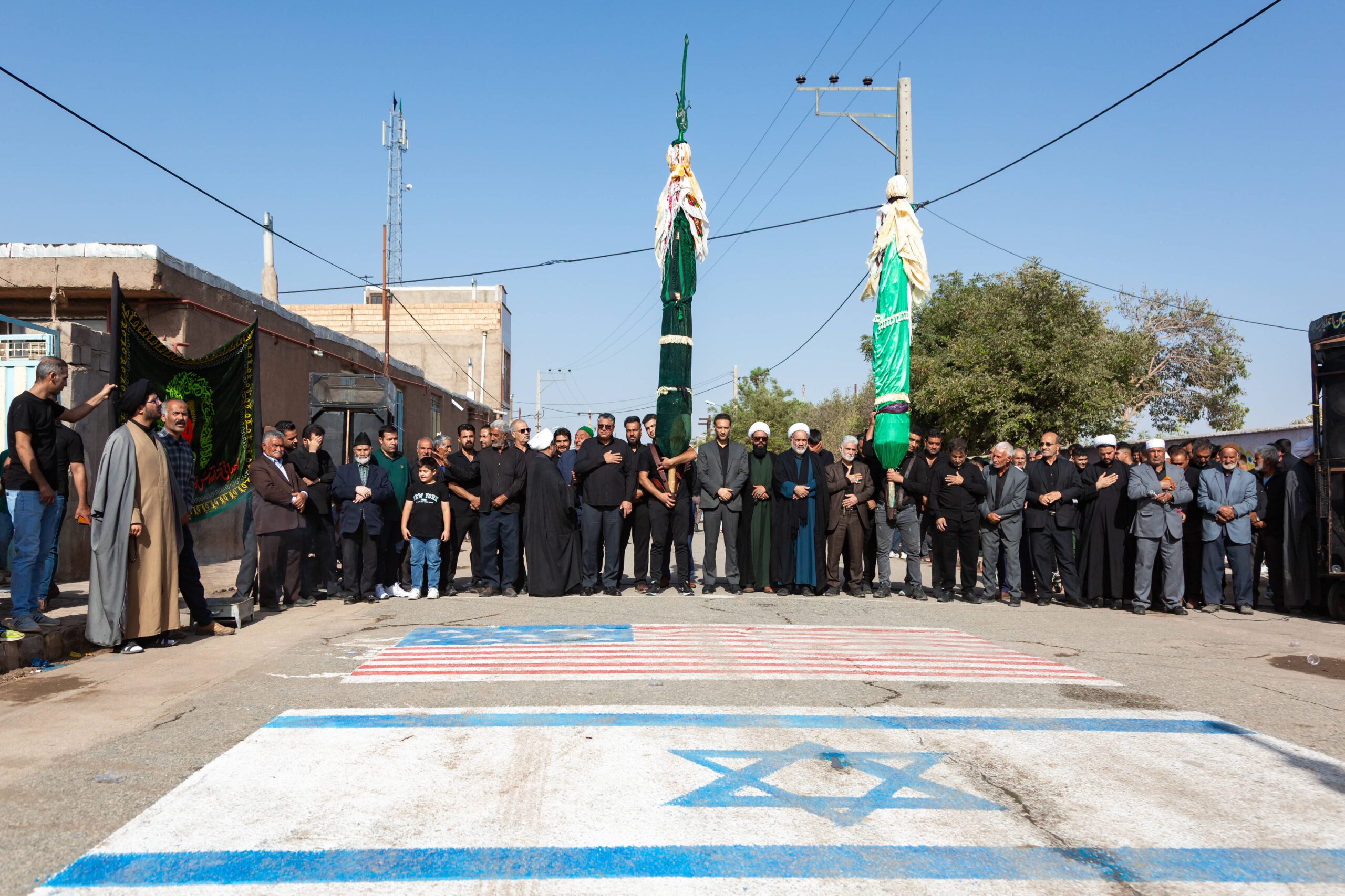 Des musulmans chiites participent aux rituels de deuil de l'Arba'in, rassemblés près d'un drapeau israélien et américain peint sur une rue du village d'Ahmadabad, près de Neyshabur, en Iran, le 14 août 2025. L'Arba'in correspond au 40e jour suivant la mort de l'imam Husayn, petit-fils du prophète Mahomet, lors de la bataille de Karbala. © Morteza Aminoroayayi/MEI/SIPA