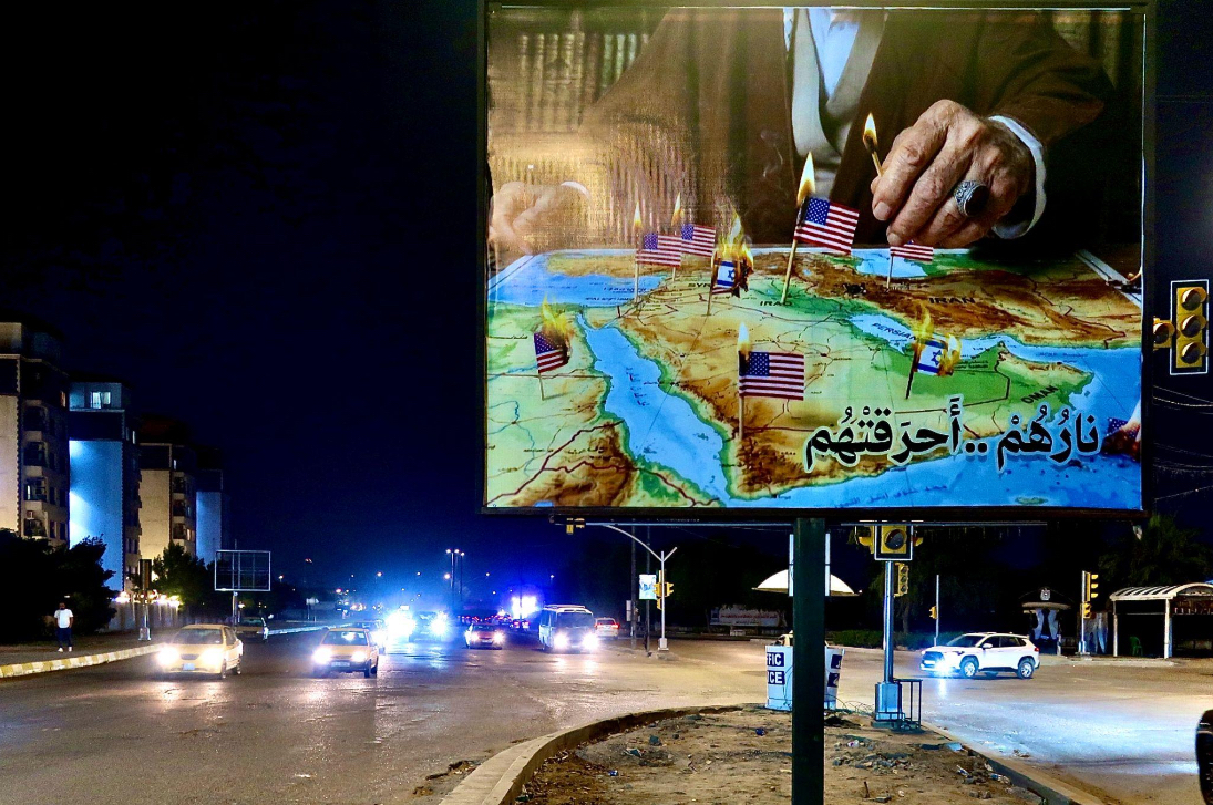 Photo datant du 2 mars 2026 d'un panneau de Baghdad avec l'inscription «Son feu les a brûlés» en arabe (Irak). Prise peu de temps après la mort de Ali Khamenei, la figure du Mahdi y met le feu aux drapeaux désignant les bases américaines et israéliennes du Golfe. © Nicolò Sancassiani