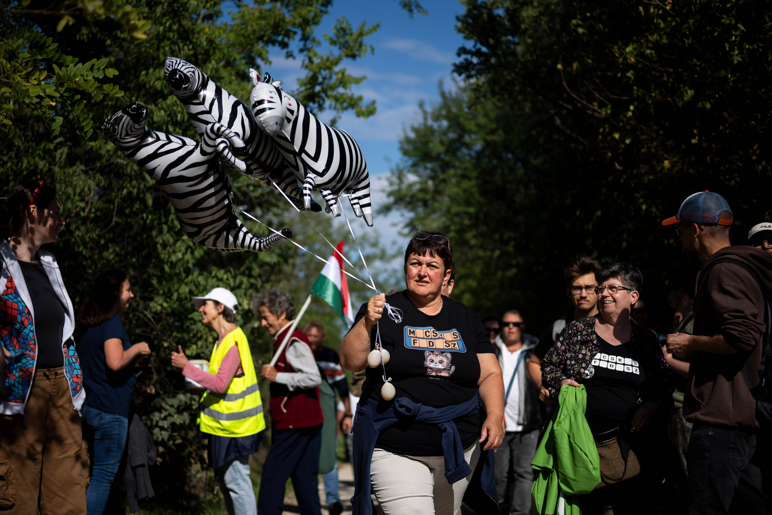 Une femme tient des ballons en forme de zèbre alors que des manifestants se rassemblent devant Hatvanpuszta, le samedi 27 septembre 2025. © Denes Erdos/AP Photo