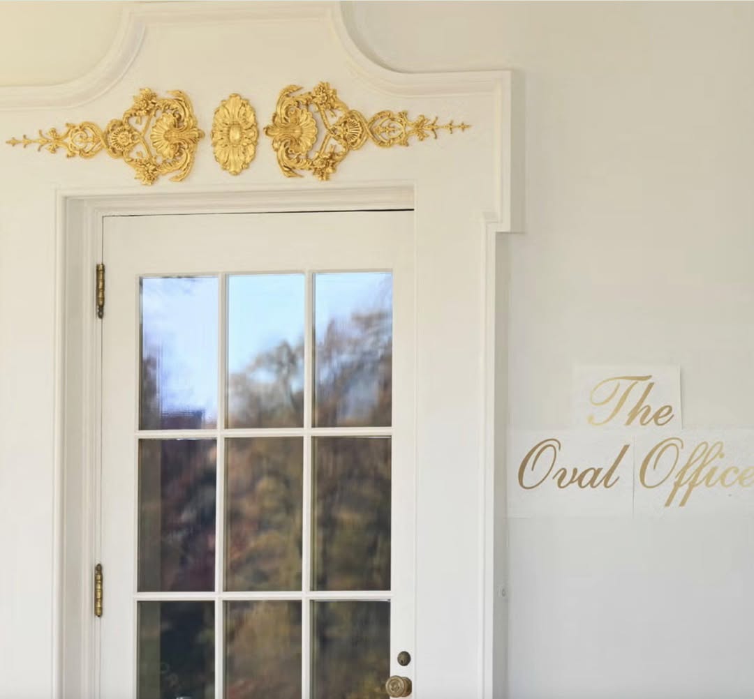La porte extérieure du Bureau ovale, sous la colonnade, ornements rocaille dorés au-dessus du chambranle et, sur le mur, l'inscription «The Oval Office» en lettres cursives dorées — appliquées sur des feuilles de papier dont les bords, encore visibles, se décollent du mur. Photo officielle
