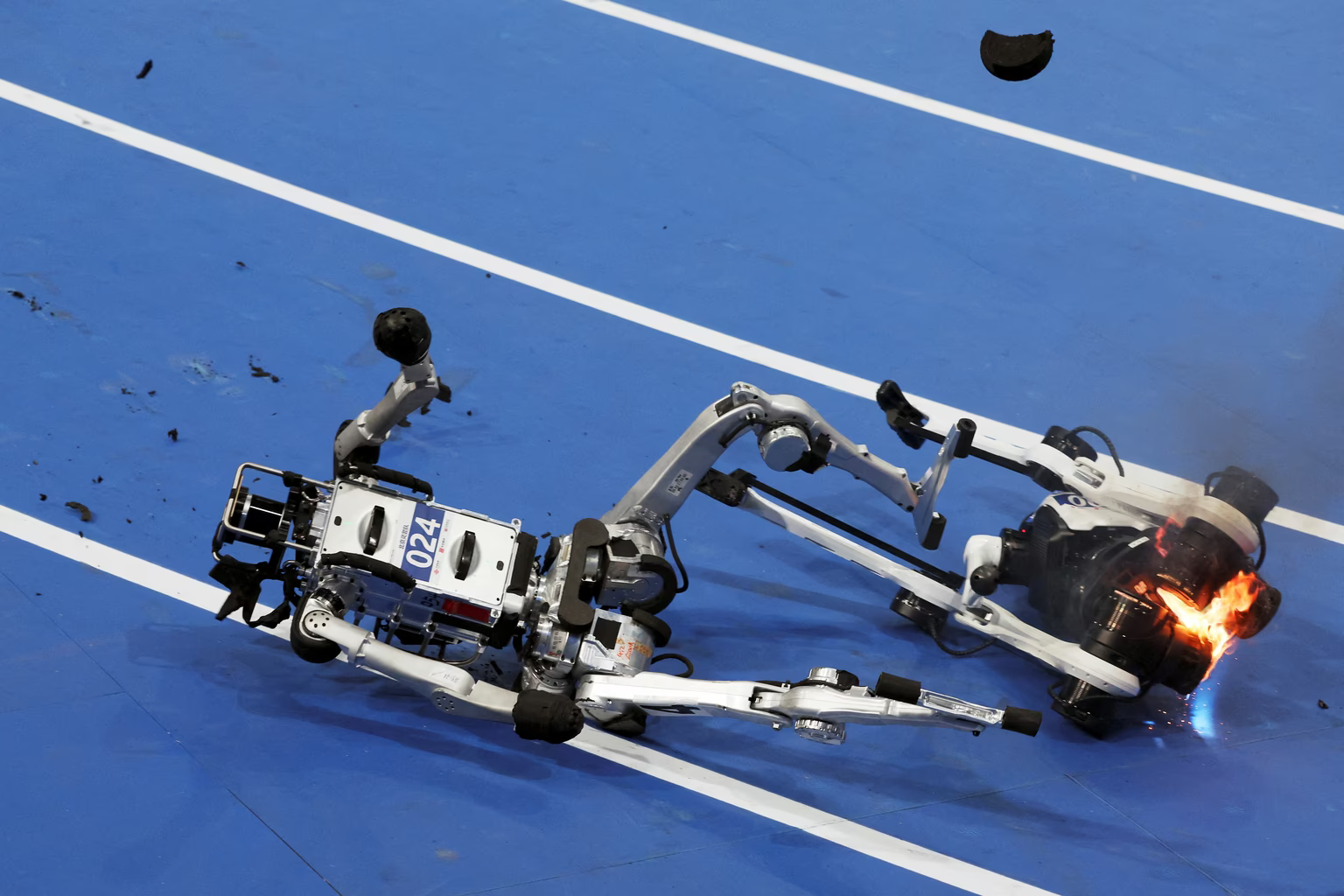 Un robot chute à côté d'un autre robot en flammes après avoir terminé la course préliminaire par groupes de 100 mètres pour les robots de grande taille.