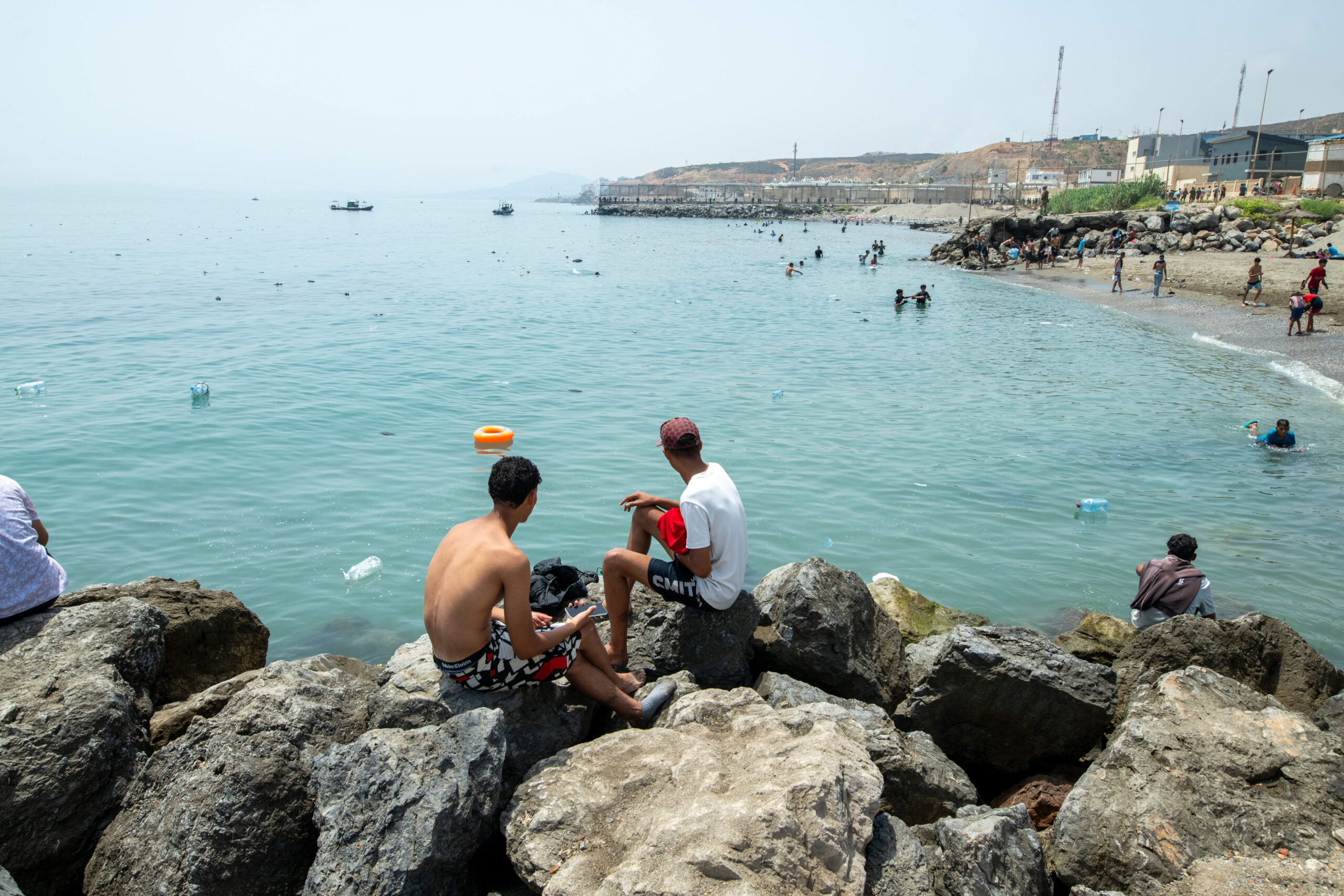 Depuis les rochers, de jeunes marocains contemplent une baie qui ressemble à n'importe quelle plage du détroit, à ceci près que le grillage frontalier, au fond, coupe le littoral en deux et plonge dans la mer. Photo : Juan Carlos Lucas
