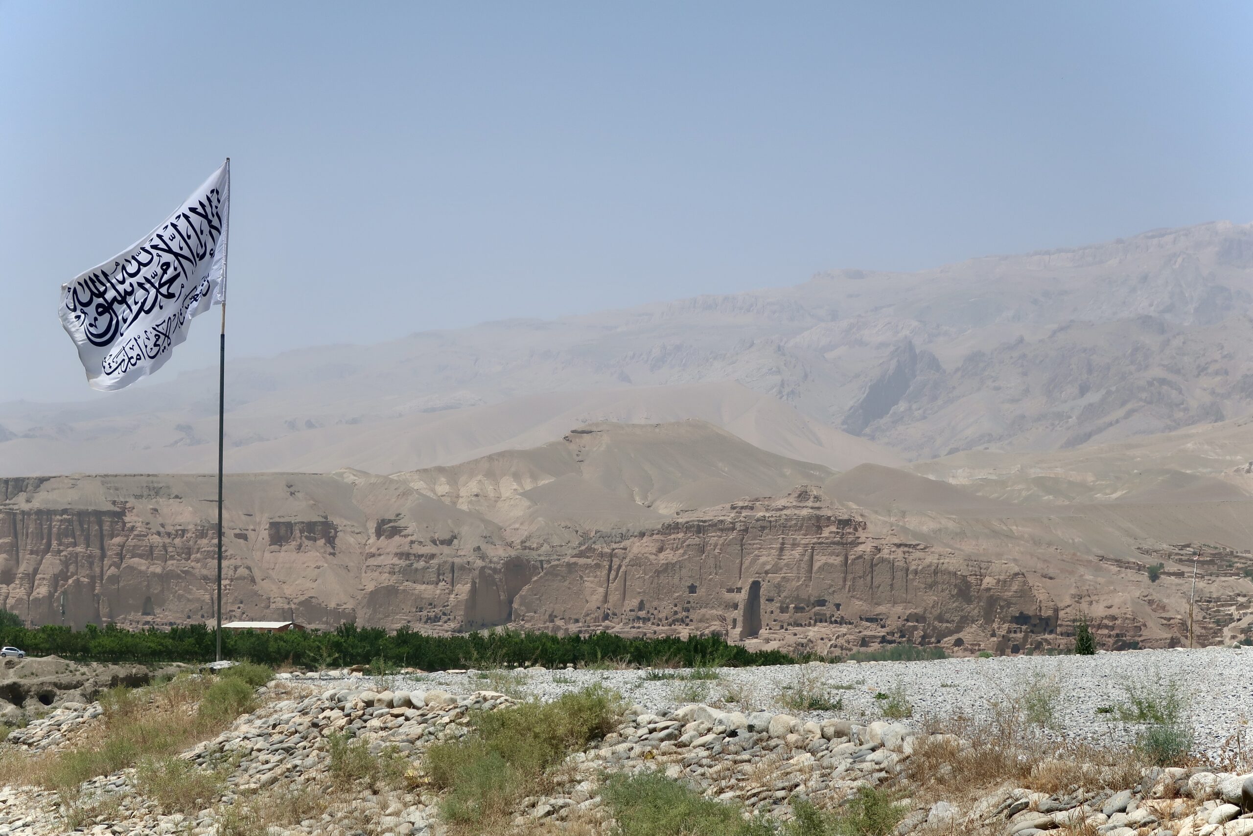 Le drapeau blanc de l'Émirat flotte devant la falaise de Bamyan. Au centre, la niche vide du grand Bouddha, dynamité par les talibans en mars 2001. Le site figure aujourd'hui dans les circuits touristiques promus par le régime. © Nicolò Sancassiani