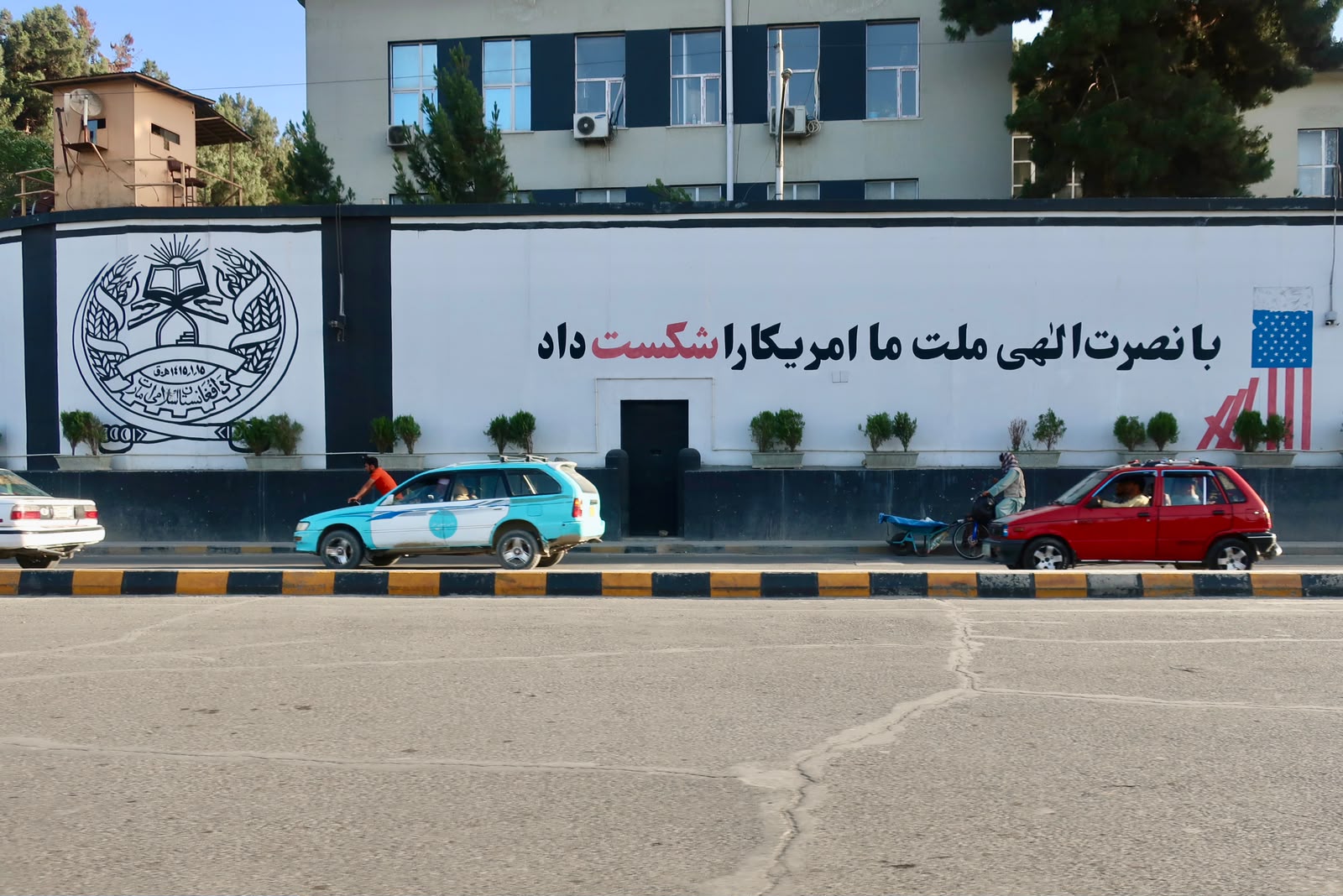 Le mur d'enceinte de l'ancienne ambassade des États-Unis à Kaboul. À gauche, l'emblème de l'Émirat islamique, à droite, un drapeau américain brisé et l'inscription en dari : « Avec l'aide de Dieu, notre nation a vaincu l'Amérique. ». © Nicolò Sancassiani.